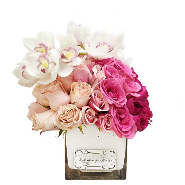 Ombre floral arrangement from light to dark pink set in square cube vase